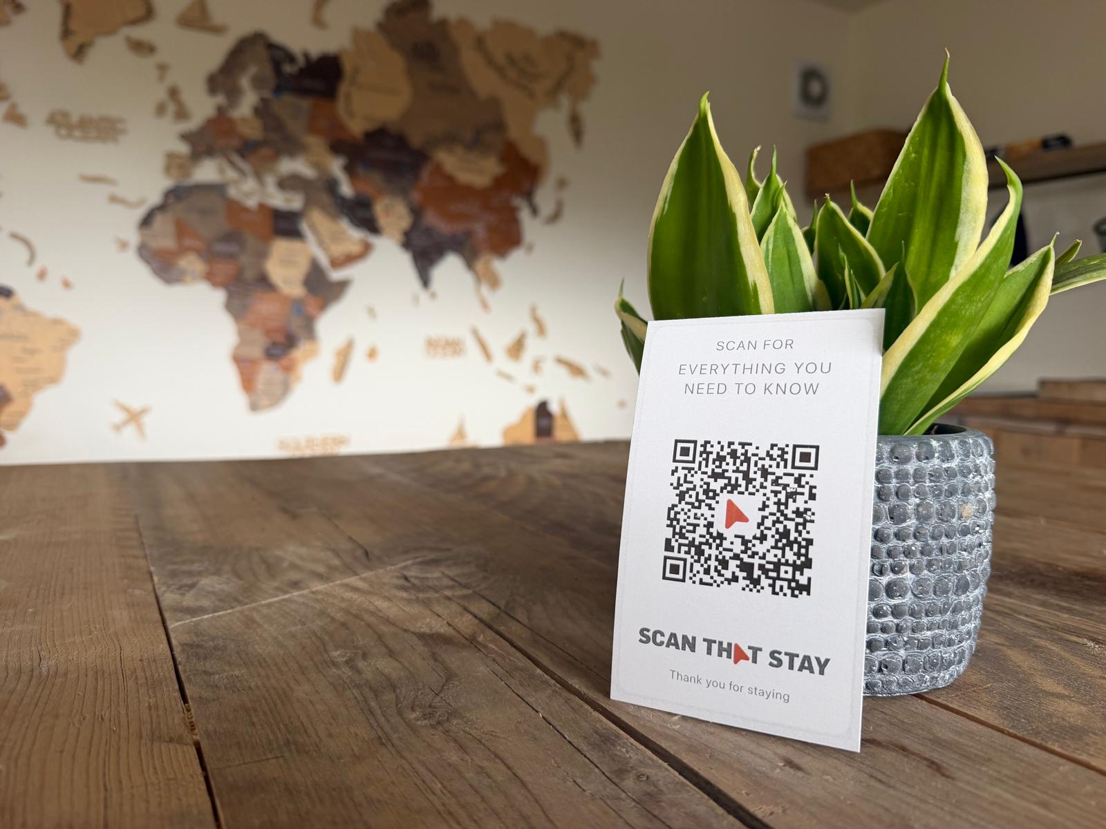 A Scan That Stay card propped against a house plant on a kitchen table, ready for guests to scan