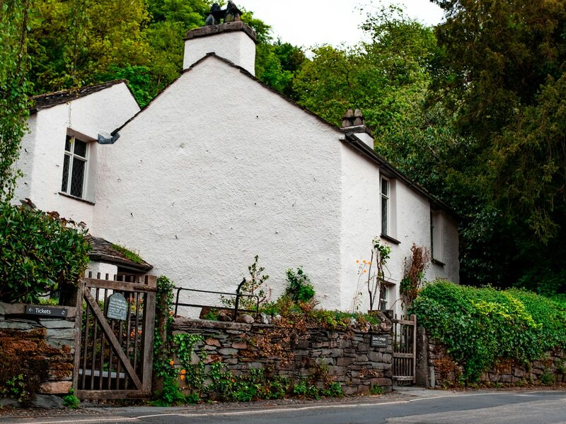 White Lakeland cottage behind a wooden gate and a dry stone wall in Ambleside