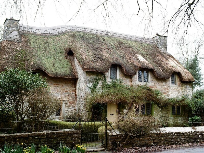 Thatched New Forest cottage behind railings and a spring garden in Beaulieu